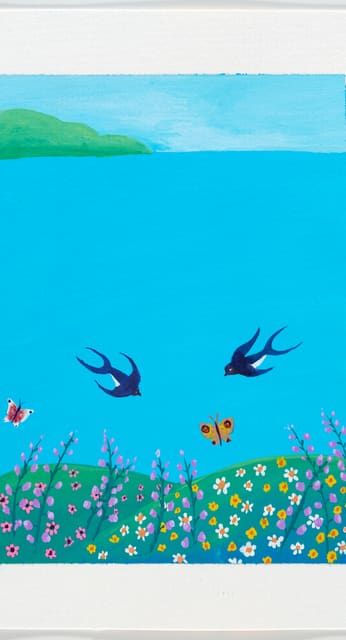 Zwei dunkle Vögel fliegen über einer türkisblauen Wasserfläche und einer blühenden Uferwiese.